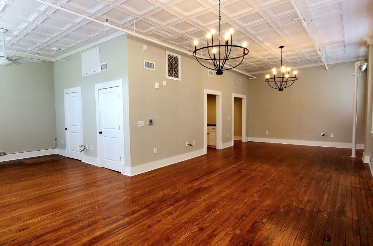 Large room with wooden floors, multiple doors to other rooms. High ceilings, and chandelier lighting.