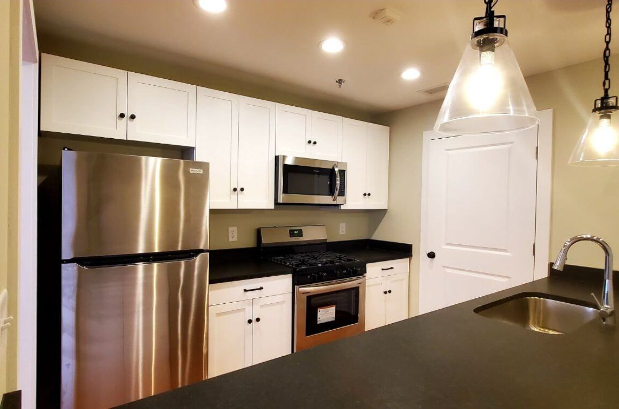 Kitchen area with a lot of counter top space around the sink. A microwave, stove, refrigerator, more counter space on the other side.