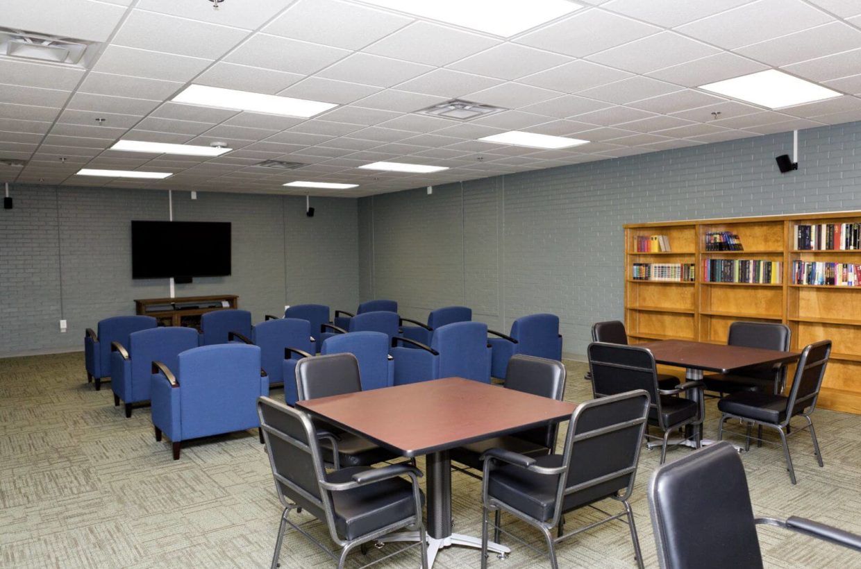 A meeting room with bookshelf, tv, tables, and chairs.