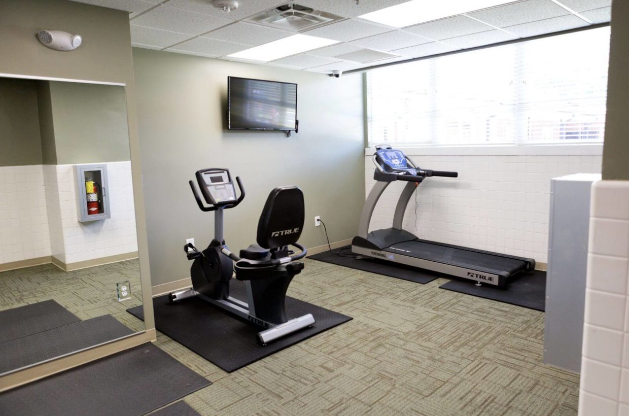An indoor gym with stationary bike and treadmill, a large window to the outside, and a tv.