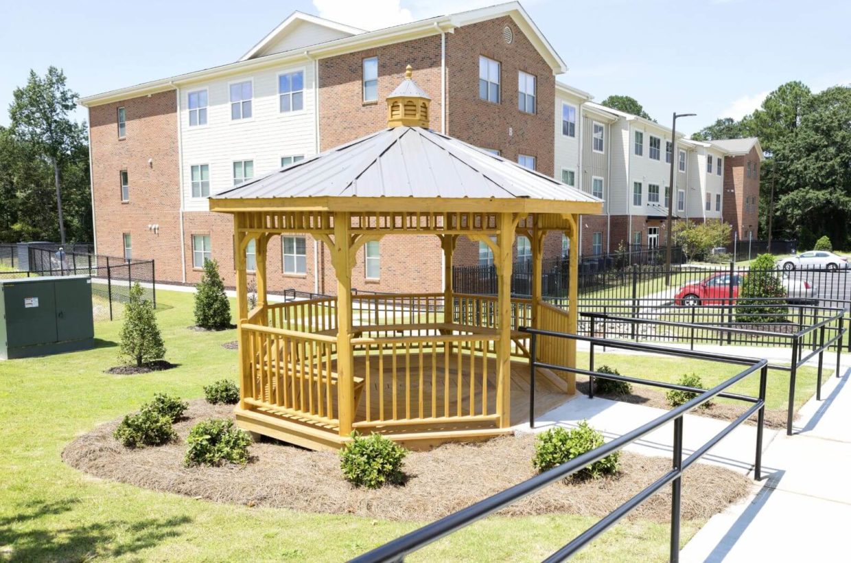 A gazeebo with bench seating outside of an apartment building.