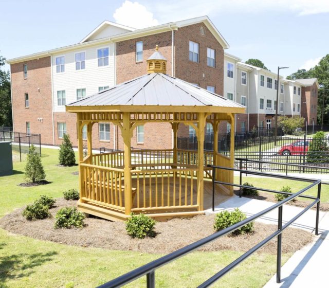 A gazeebo with bench seating outside of an apartment building.