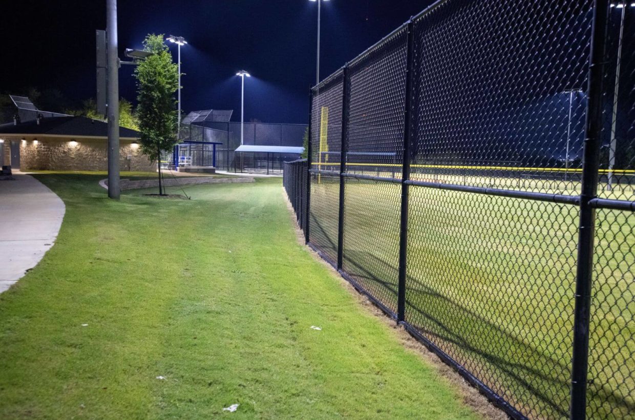 Brick and concrete walkways next to baseball fields, lit up at night.